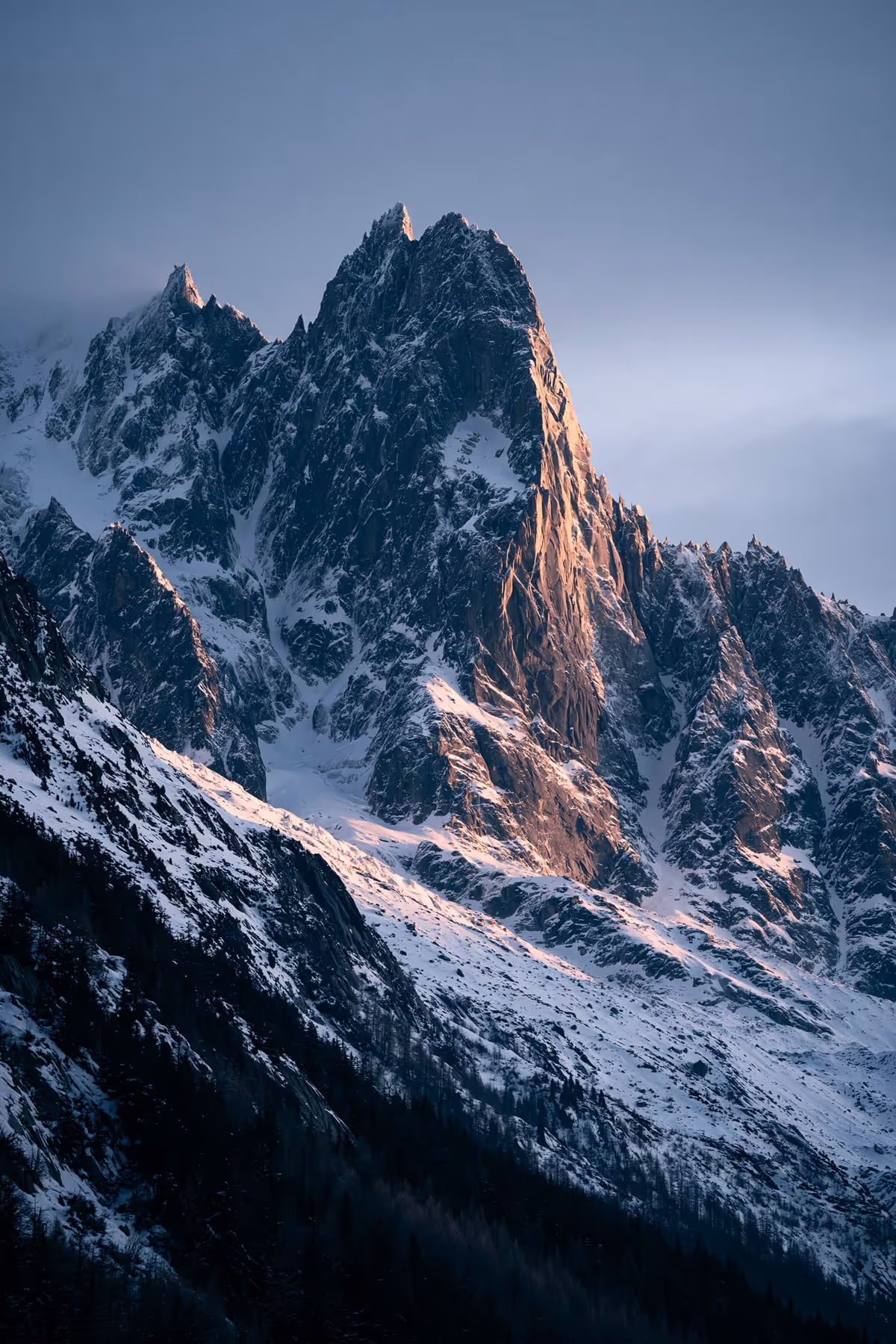 The granite spires of Mont Blanc at dawn, half in shadow and half in golden light.